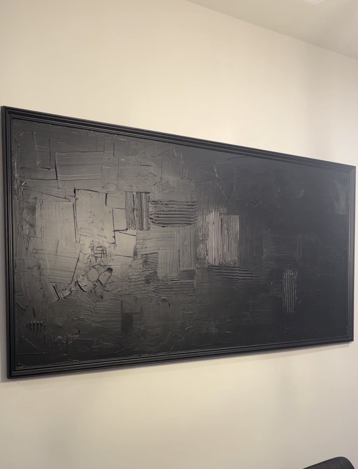 Large framed black textured art piece hanging on a wall